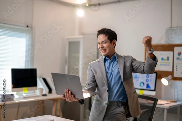 Fototapeta A man in a suit is holding a laptop and smiling