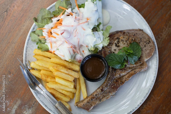 Fototapeta Black pepper pork steak with french fries and vegetable salad on a white plate