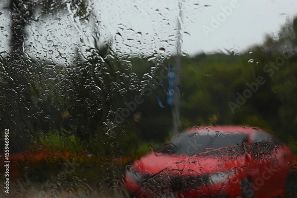 Fototapeta red car on parking in raining day, abstract blur background