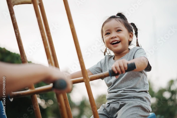 Fototapeta cheerful toddler girl playing on double swing with freind at outdoor playground