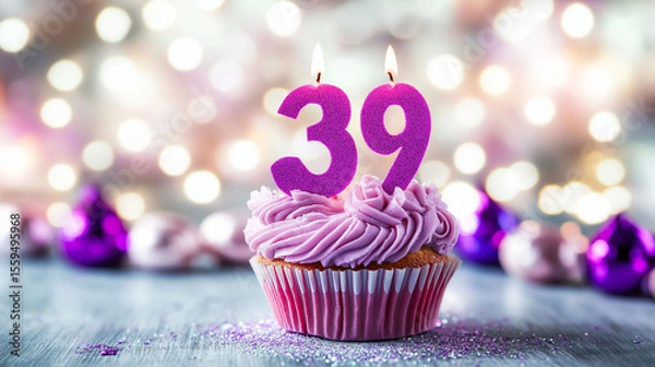 Fototapeta A pink cupcake with the number "39" in purple frosting, sitting on an elegant table against a blurred background of twinkling lights and a bokeh effect.