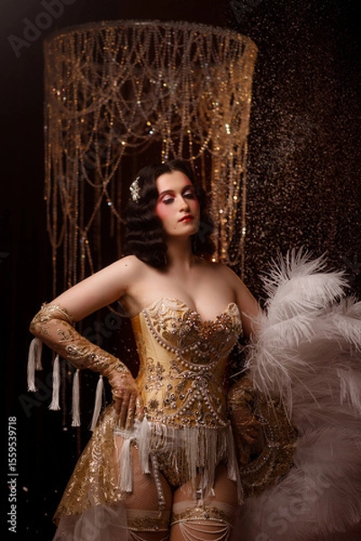 Fototapeta Young Caucasian circus performer or burlesque dancer in golden vintage corset, front view, posing under chandelier on dark background. Concepts: circus, cabaret, retro, show, performance.