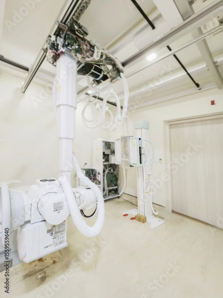 Fototapeta A high-tech X-ray machine in a medical room, featuring advanced equipment and intricate wiring. It’s ready to provide clear and detailed imaging for diagnostics.