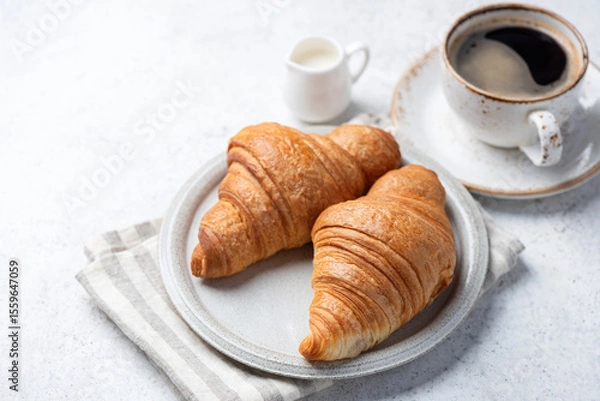 Fototapeta Two croissants and cup of black coffee on light grey concrete background, concept of breakfast and bakery food, copy space