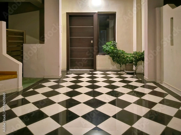 Obraz Modern entrance featuring a wooden door with horizontal metal strips, window, and potted plant. The floor is adorned with black and white checkered pattern, and space is illuminated by ceiling light.