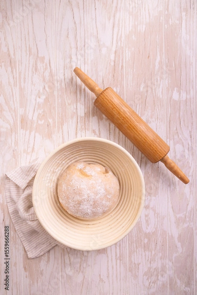 Obraz Raw yeast dough with rolling pin resting and rising in a special basket