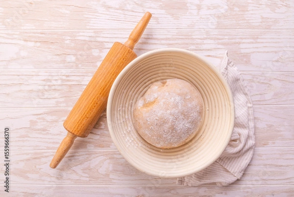 Obraz Raw yeast dough with rolling pin resting and rising in a special basket