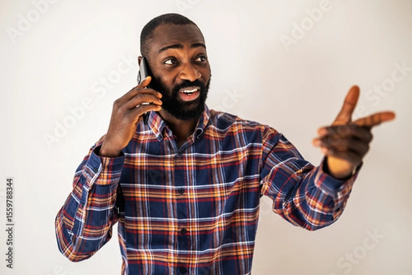 Fototapeta Cheerful black man in cozy shirt standing in front of wall and talking on mobile phone.