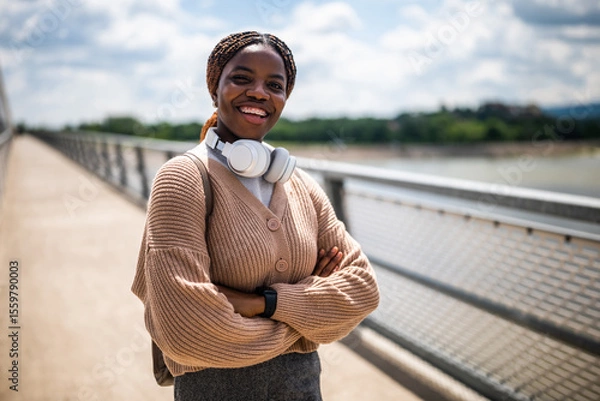 Fototapeta Happy young black woman is looking at camera and smiling. She is enjoying sunny day outdoor.