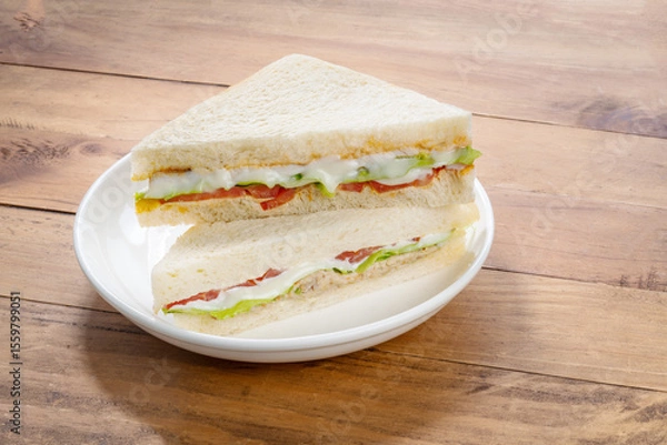 Obraz Sandwich with fresh vegetables and creamy salad dressing on white plate isolete on wooden background .