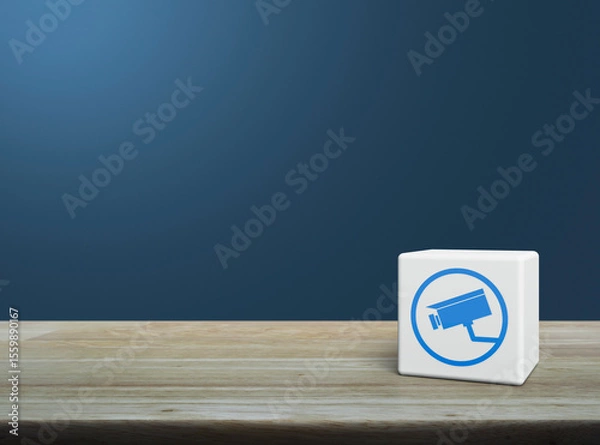 Fototapeta Cctv camera flat icon on white block cube on wooden table over light blue wall, Technology security and safety online concept