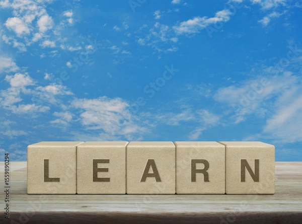 Fototapeta Learn letter on wood block cubes on wooden table over blue sky with white clouds, Business, education and learning concept