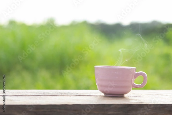 Obraz Hot coffee cup on wooden table in the garden, green leaves blurred as background, pink coffee cup