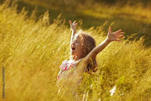 Fototapeta Happy little girl in tall grass in a field on a summer evening.