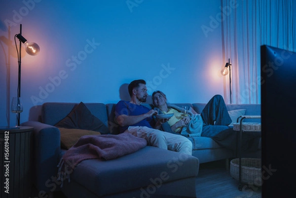 Obraz Couple watching TV at night  while sharing a bowl of popcorn and wine on sofa