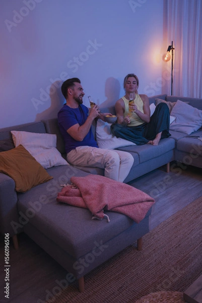 Obraz Couple sitting on a couch, enjoying beer and nachos in a cozy living room