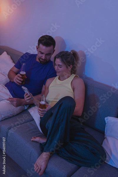 Obraz  Couple Sitting on Couch with Drinks and Smartphone During Cozy Evening at Home