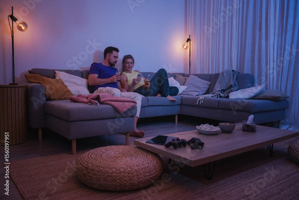Obraz  Couple Sitting on Couch with Drinks and Smartphone During Cozy Evening at Home