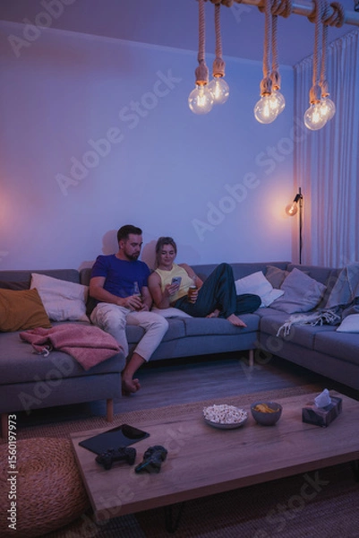 Obraz  Couple Sitting on Couch with Drinks and Smartphone During Cozy Evening at Home
