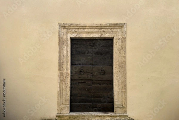 Fototapeta minimalist image of a vintage wooden door with stone frame on light beige wall. historical elegance architectural concept with empty