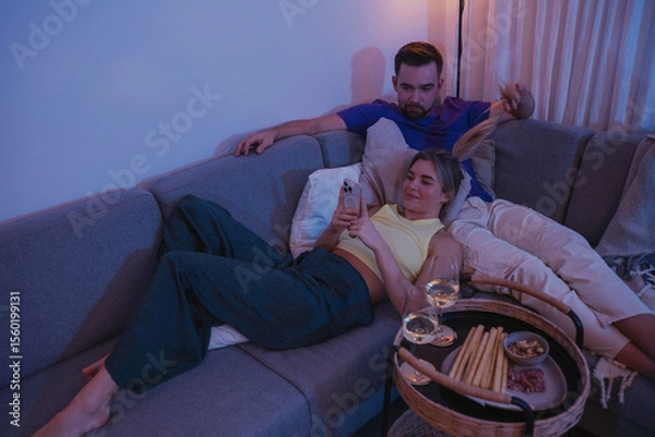 Obraz  Couple Relaxing on Sofa at Night Using Smartphones with Snacks and Wine