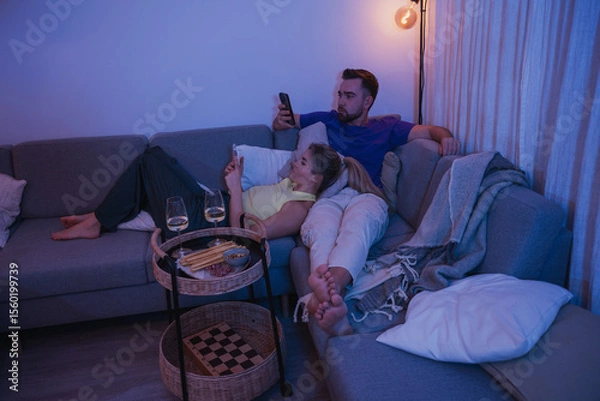 Obraz  Couple Relaxing on Sofa at Night Using Smartphones with Snacks and Wine