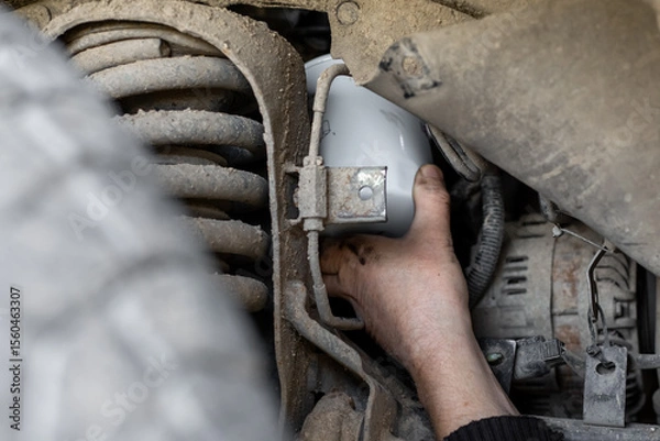 Fototapeta Mechanic's hand reaches out to install or remove an oil filter on the underbody of a car. Changing an oil filter