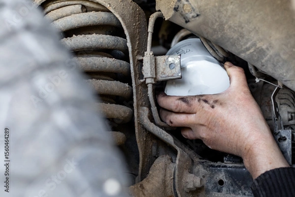Fototapeta Mechanic's hand reaches out to install or remove an oil filter on the underbody of a car. Changing an oil filter