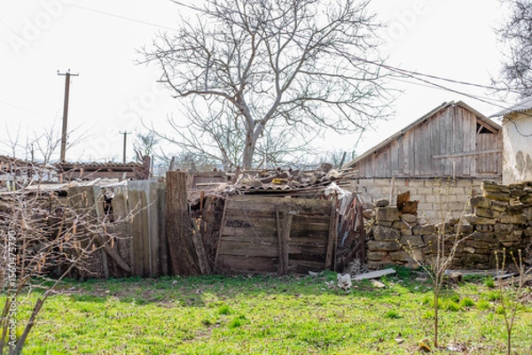 Fototapeta Scene of desolation with crumbling building and overgrown foliage in rural area. Old house and barns in village