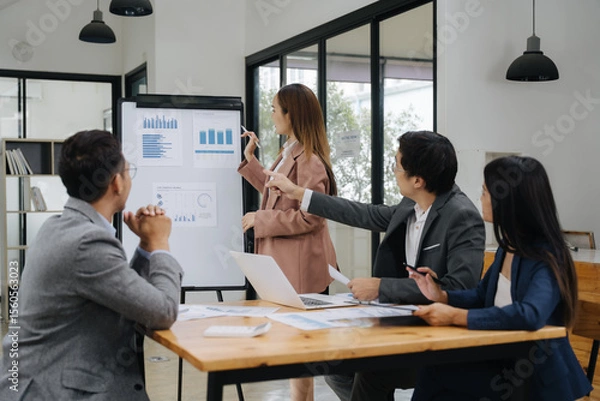 Fototapeta Business Collaboration: A team of professionals intently examines data on a flip chart during a business presentation, a collaborative effort.