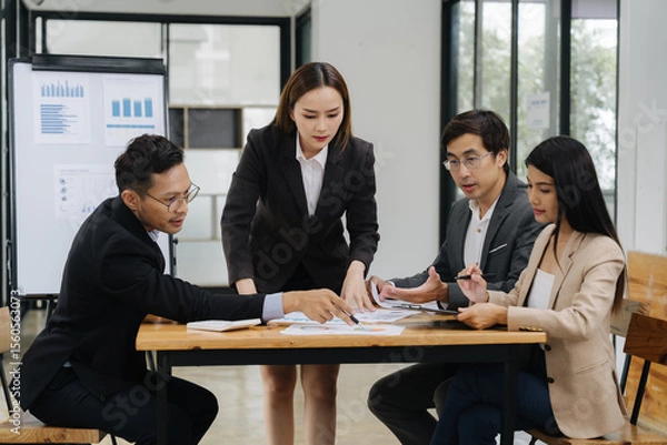Fototapeta Strategic Discussions: A dynamic team of professionals huddle around a desk, engaging in a deep discussion about data, planning, and collaboration. Capturing the essence of workplace synergy