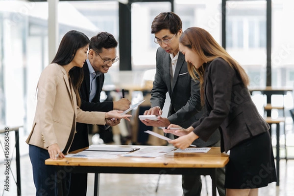 Fototapeta Collaborative Analysis: A team of focused business professionals huddles over documents and a calculator, engaged in an intense analysis of data.