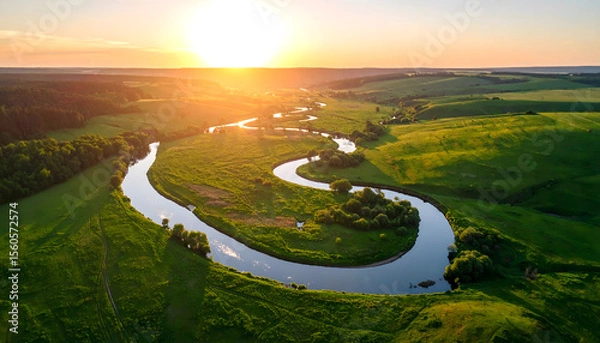 Fototapeta Winding river reflecting golden hues of sunset meandering through lush green fields, creating serene landscape