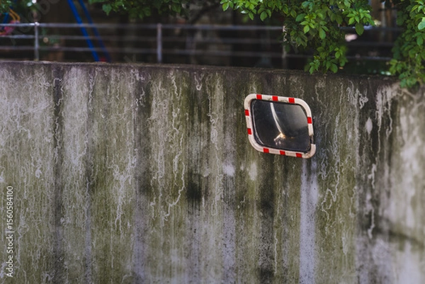 Fototapeta Mirror reflects a quiet park corner with weathered wall and lush greenery in the late afternoon light