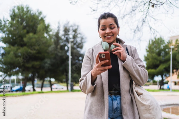 Fototapeta Young woman creating content for social media using a smartphone in a city park