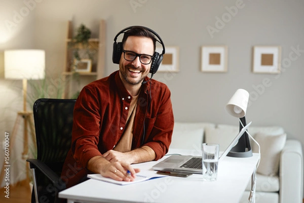 Obraz Smiling teacher wearing headset teaching online lesson and writing notes