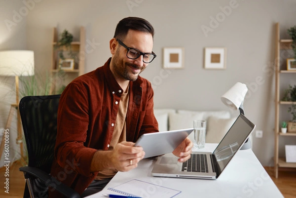 Obraz Smiling freelancer working from home using laptop and tablet