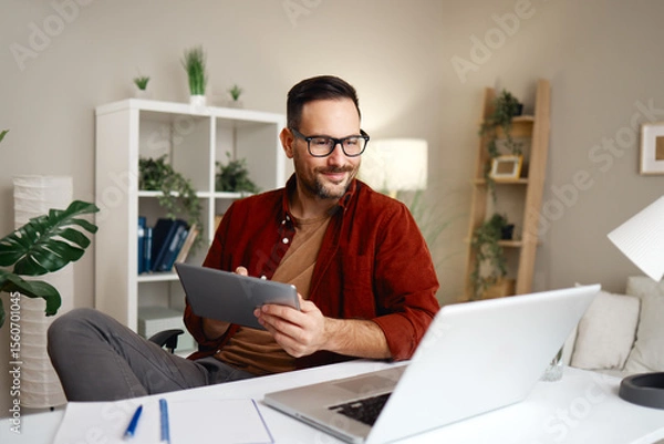 Obraz Freelancer working from home using laptop and tablet smiling