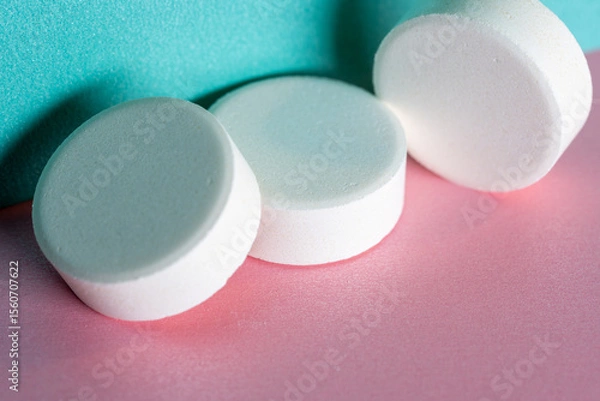 Obraz Three white medicine tablets laying unordered isolated on pink and blue pastel background as macro