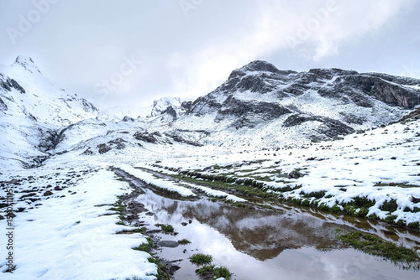 Fototapeta an image of the early spring thaw with a large puddle in the foreground reflecting the snow-capped mountaintop in the background