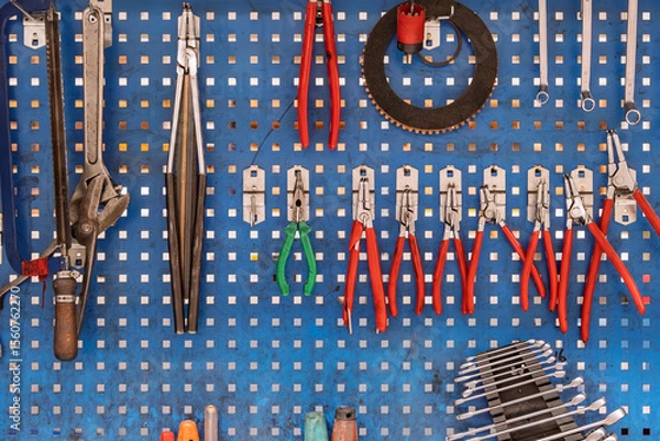 Fototapeta Wall-mounted tool set on pegboard in workshop. Old hand tools is displayed on perforated metal pegboard in a workshop setting. Use for themes related to maintenance and craftsmanship.