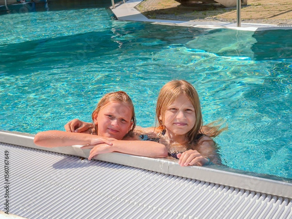 Fototapeta Two cheerful girls are happily enjoying summer fun together, splashing in a refreshing pool