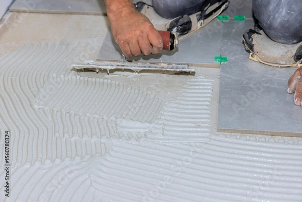 Fototapeta Worker skillfully spreads tile adhesive on floor surface for home renovation project.