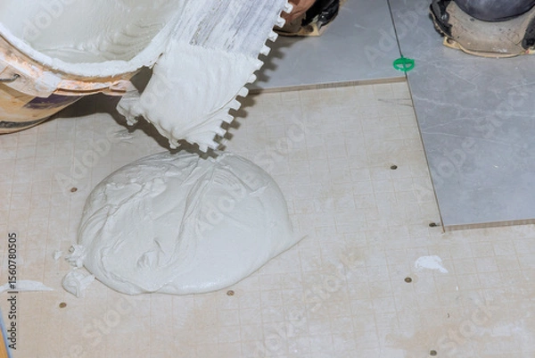 Fototapeta Worker spreads drying mortar on floor in preparation for tile installation in newly renovated space.