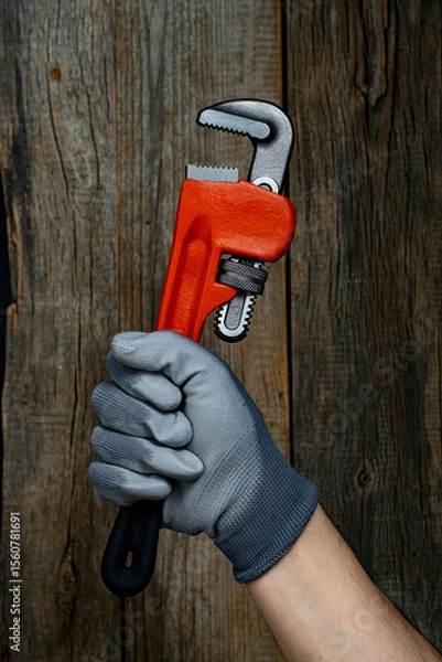 Obraz Adjustable pipe wrench in hand worker on wooden background.