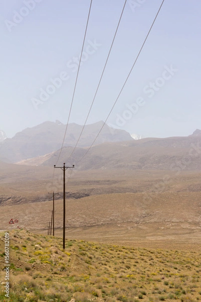 Fototapeta High-voltage power lines cut through Yazd’s arid landscape, framed by distant mountains and barren terrain under a clear desert sky.