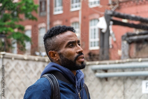 Obraz Portrait of a serious adult African American ethnicity man with a beard and glasses. A serious confident black guy a blue jacket posing. Portrait of a black man from Sudan on the blurred background. 