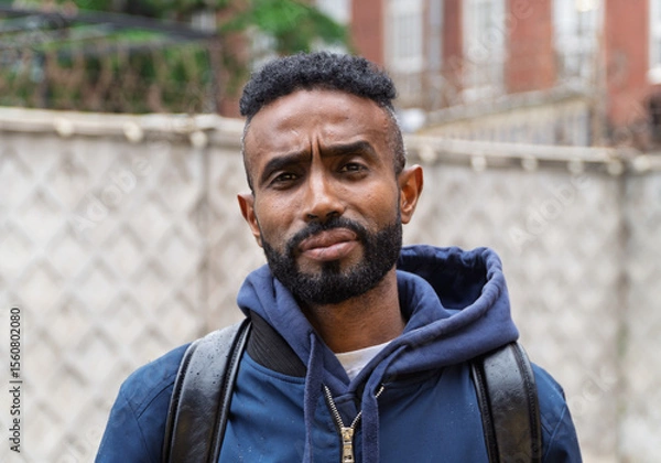 Obraz Portrait of a serious adult African American ethnicity man with a beard and glasses. A serious confident black guy a blue jacket posing. Portrait of a black man from Sudan on the blurred background. 