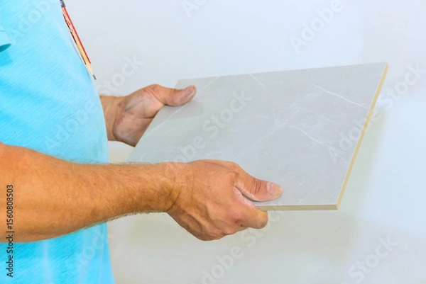 Fototapeta Someone is carefully holding gray tile, ready to be used in home renovation project during works day.