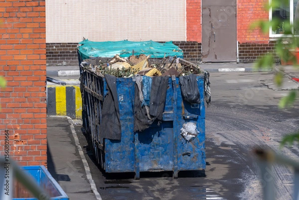 Fototapeta Filled blue dumpster with mixed garbage, on the territory of some factory. Concept of waste utilization and environmental pollution